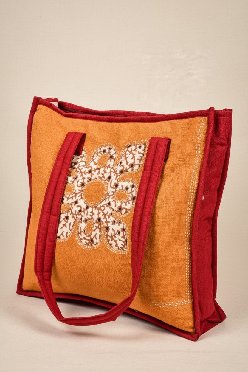 Orange tote bag with red handles and floral embroidery on a beige background