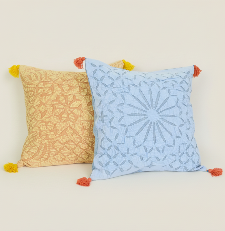 Two decorative pillows with patterns and pom-poms on a plain background