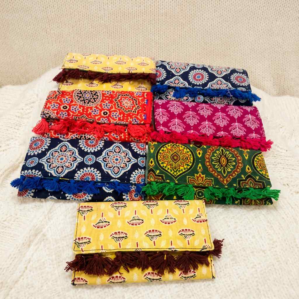 Stack of colorful ajrakh print pouches with patterns and tassels on a white surface