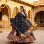 Woman in a colorful traditional outfit with a dark black applique dupatta in front of an ornate building.