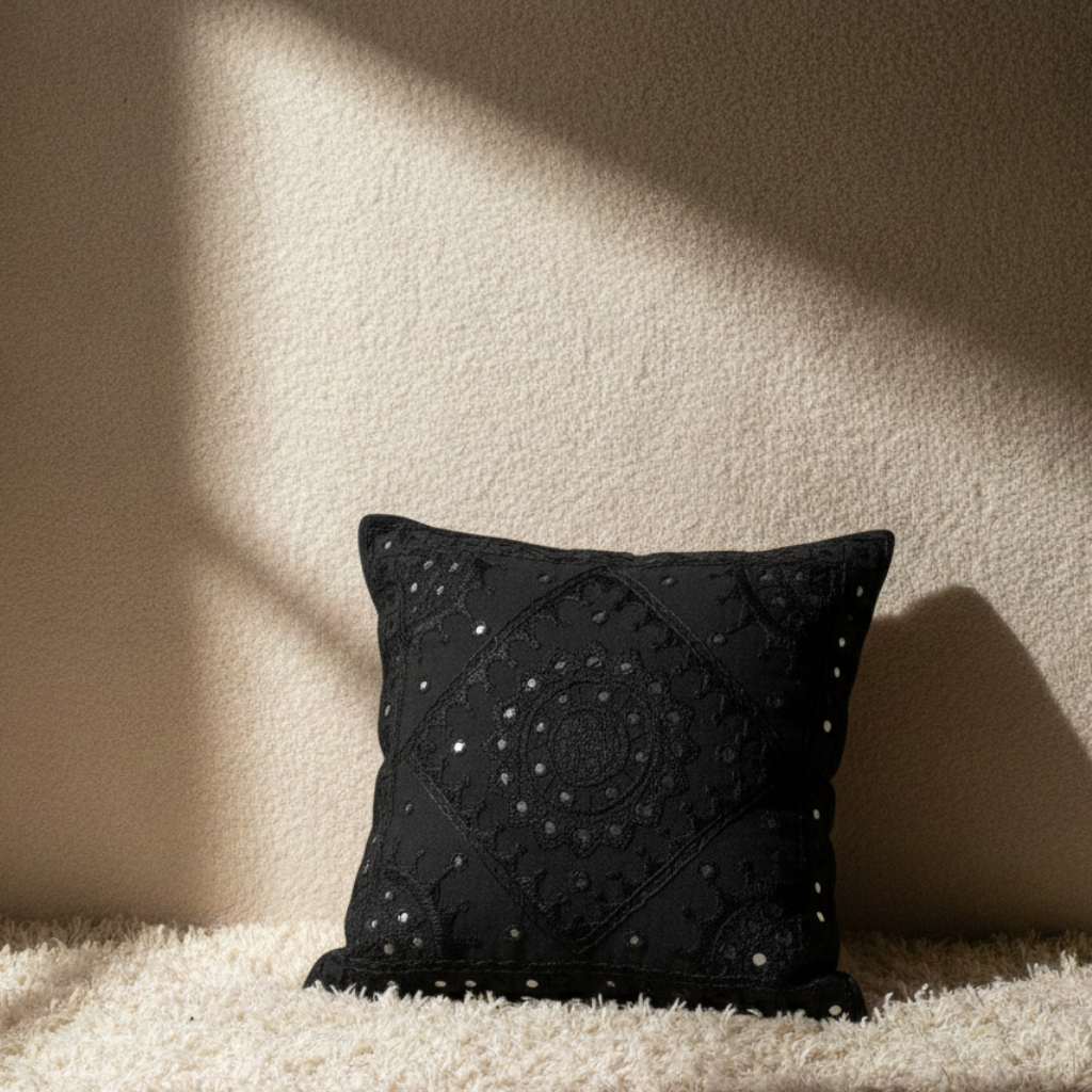 Black embroidered cushion cover on a textured surface with a neutral background