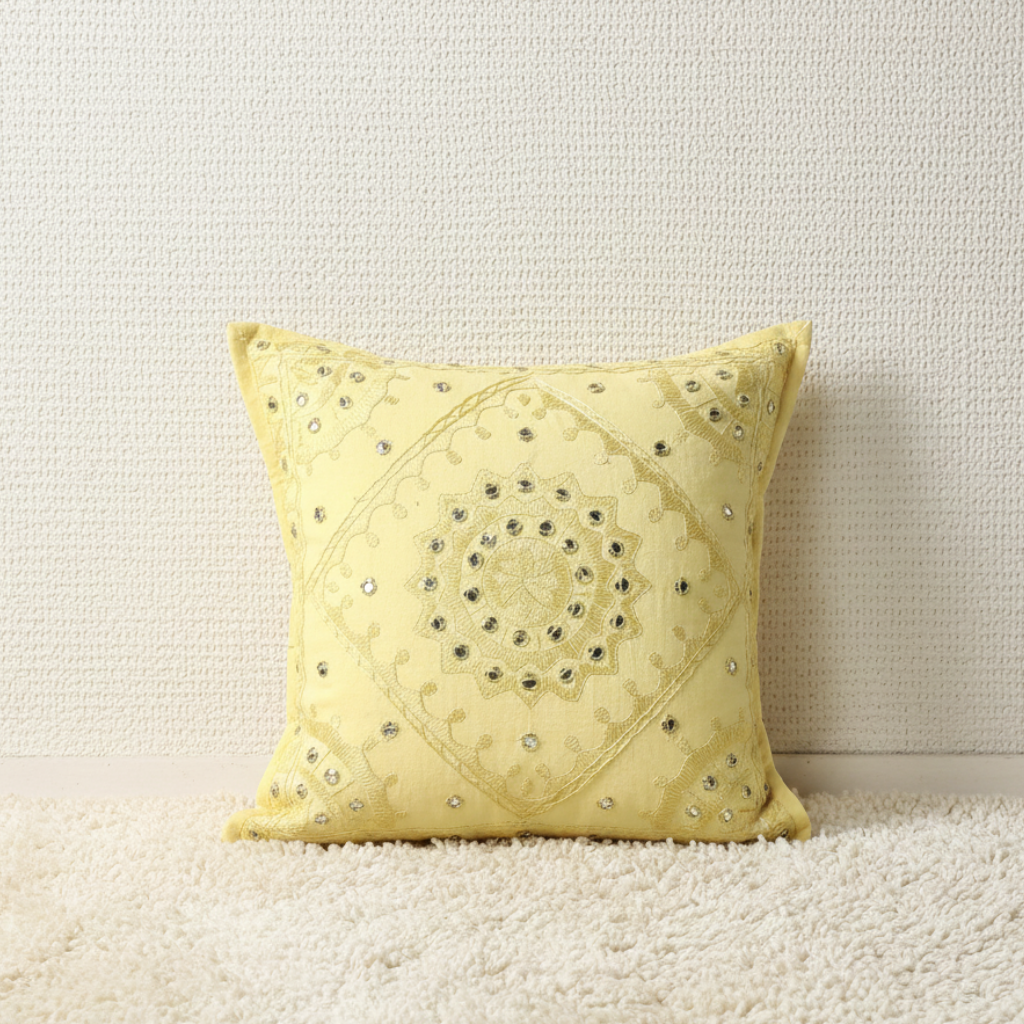 Yellow decorative cushion cover with intricate patterns on a neutral background