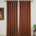 Brown curtains with grommets on a white wall with a Buddha statue and plant in the background.