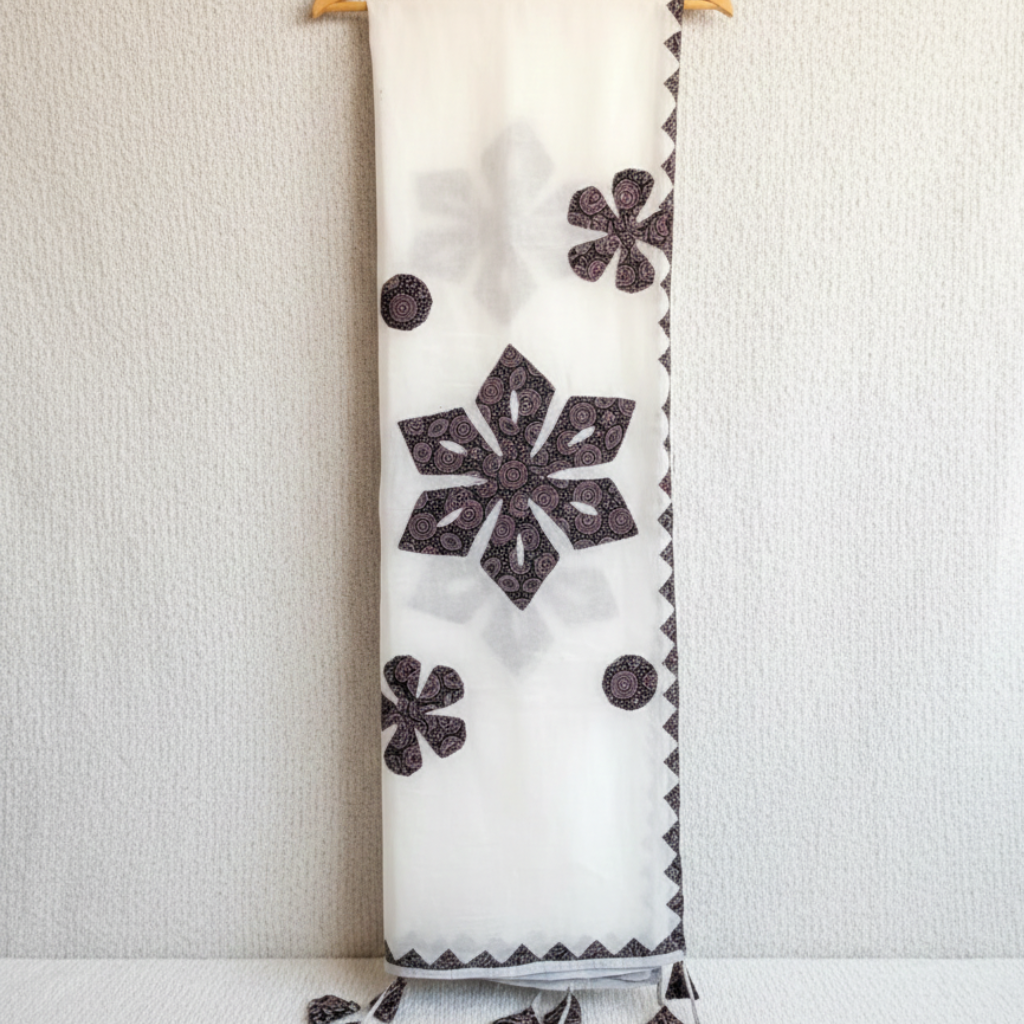 White dupatta with black floral ajrakh patterns hanging on a wooden rod against a white wall.