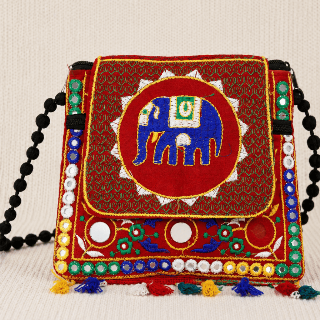 Colorful embroidered red sling bag with an elephant design on a beige background