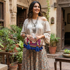 Woman holding a colorful handbag in an outdoor setting with plants and traditional architecture.
