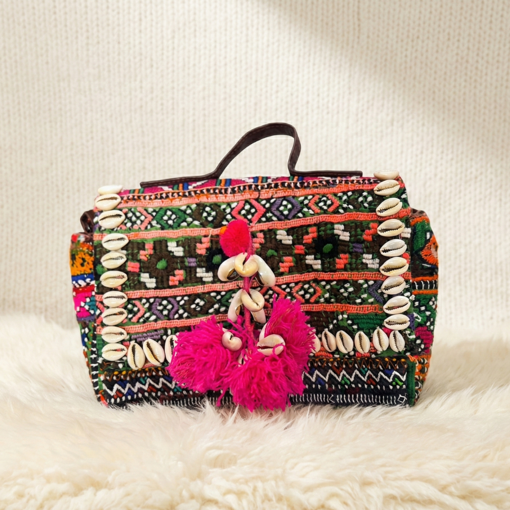Colorful banjara handbag with tribal patterns and pink tassels on a white surface