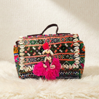 Colorful banjara handbag with tribal patterns and pink tassels on a white surface