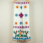 Colorful applique dupatta with floral and tree designs hanging on a wooden hanger against a beige wall.