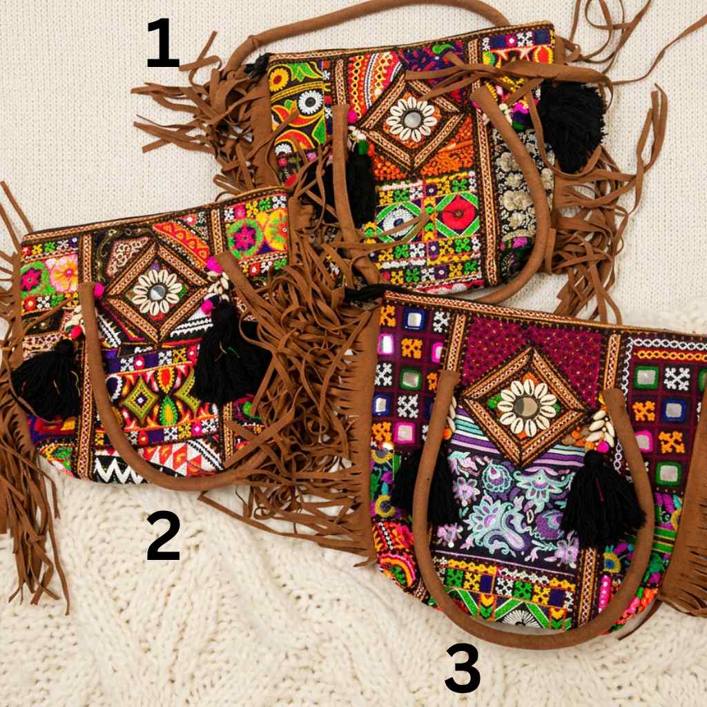 Three colorful banjara tote bags with intricate patterns and fringes on a textured surface.