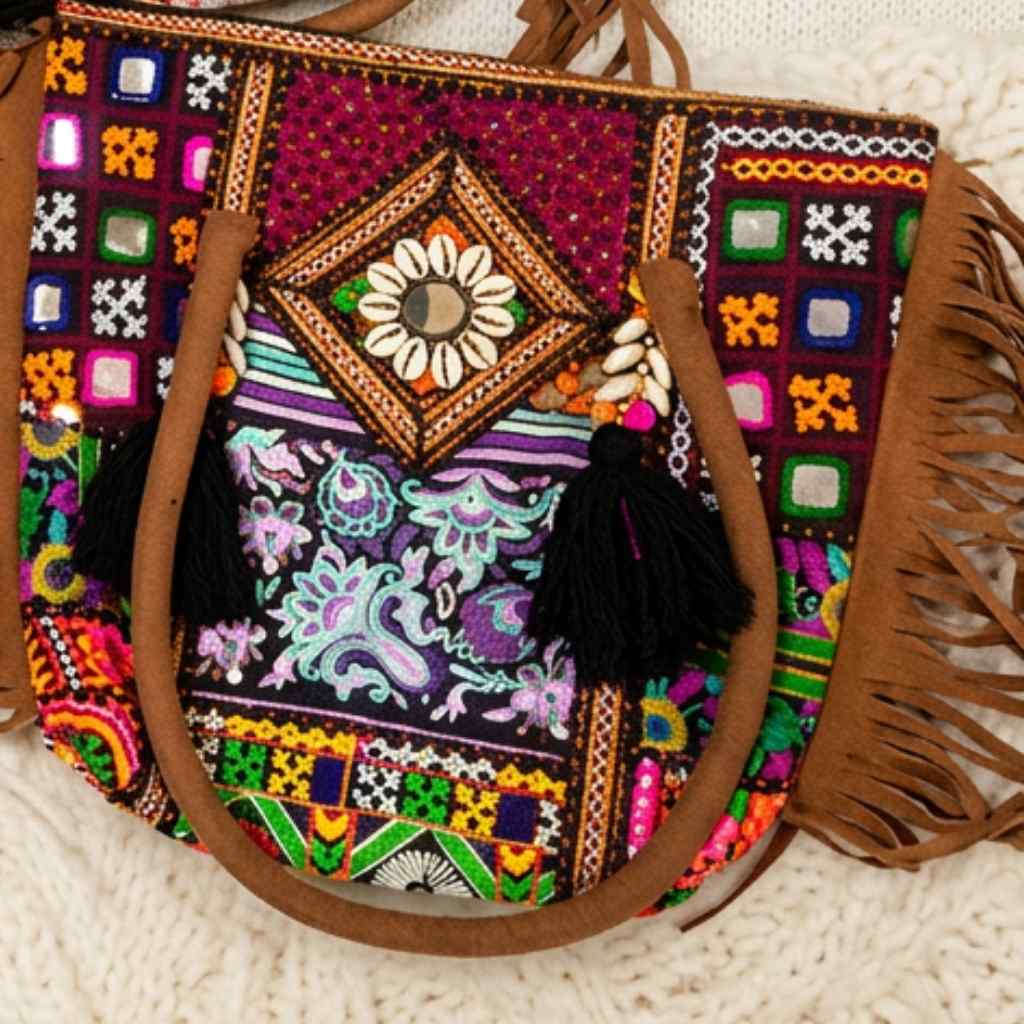 Colorful embroidered banjara tote bagwith tassels on a textured surface