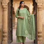 Woman in a green traditional outfit standing in front of an architectural entrance.