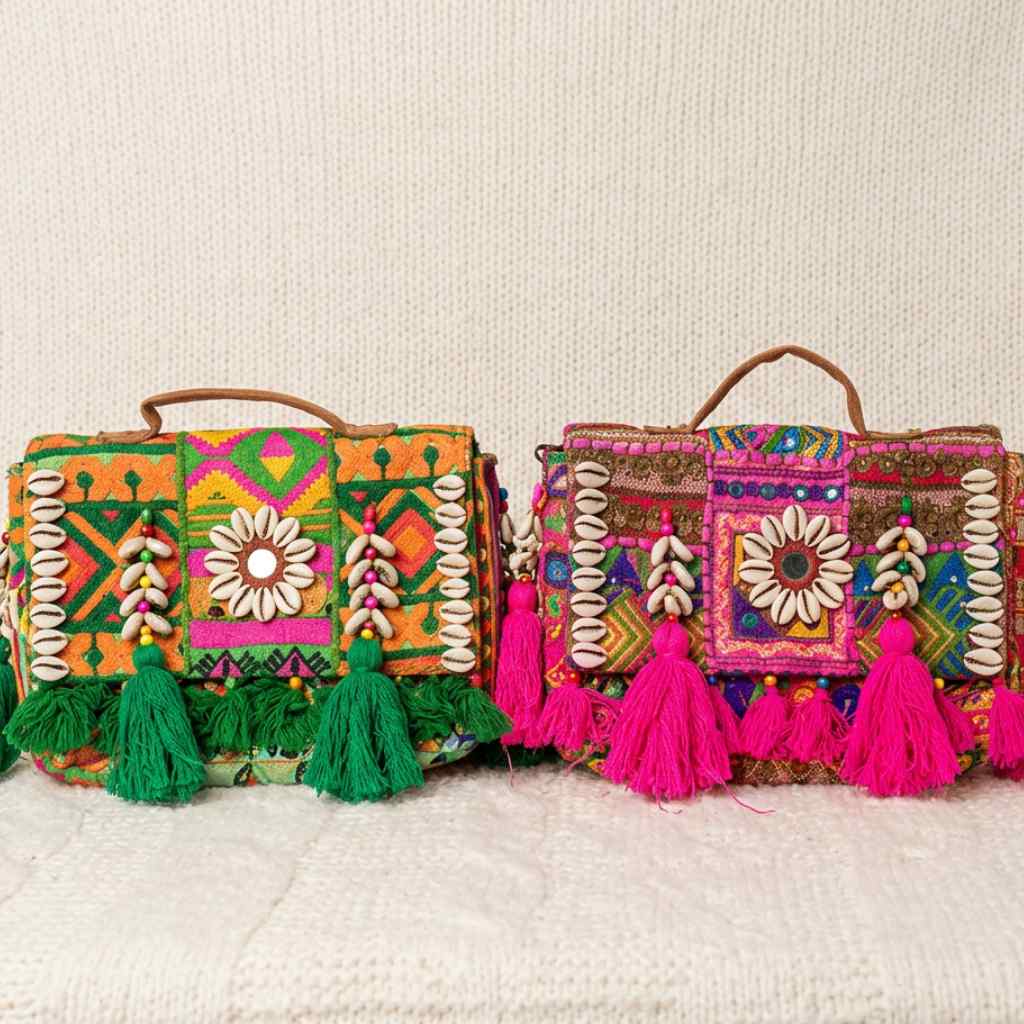 Two colorful banjara bagss in pink and green color with tassels on a textured surface