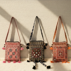 Three embroidered small sling bags with tassels on a textured beige background
