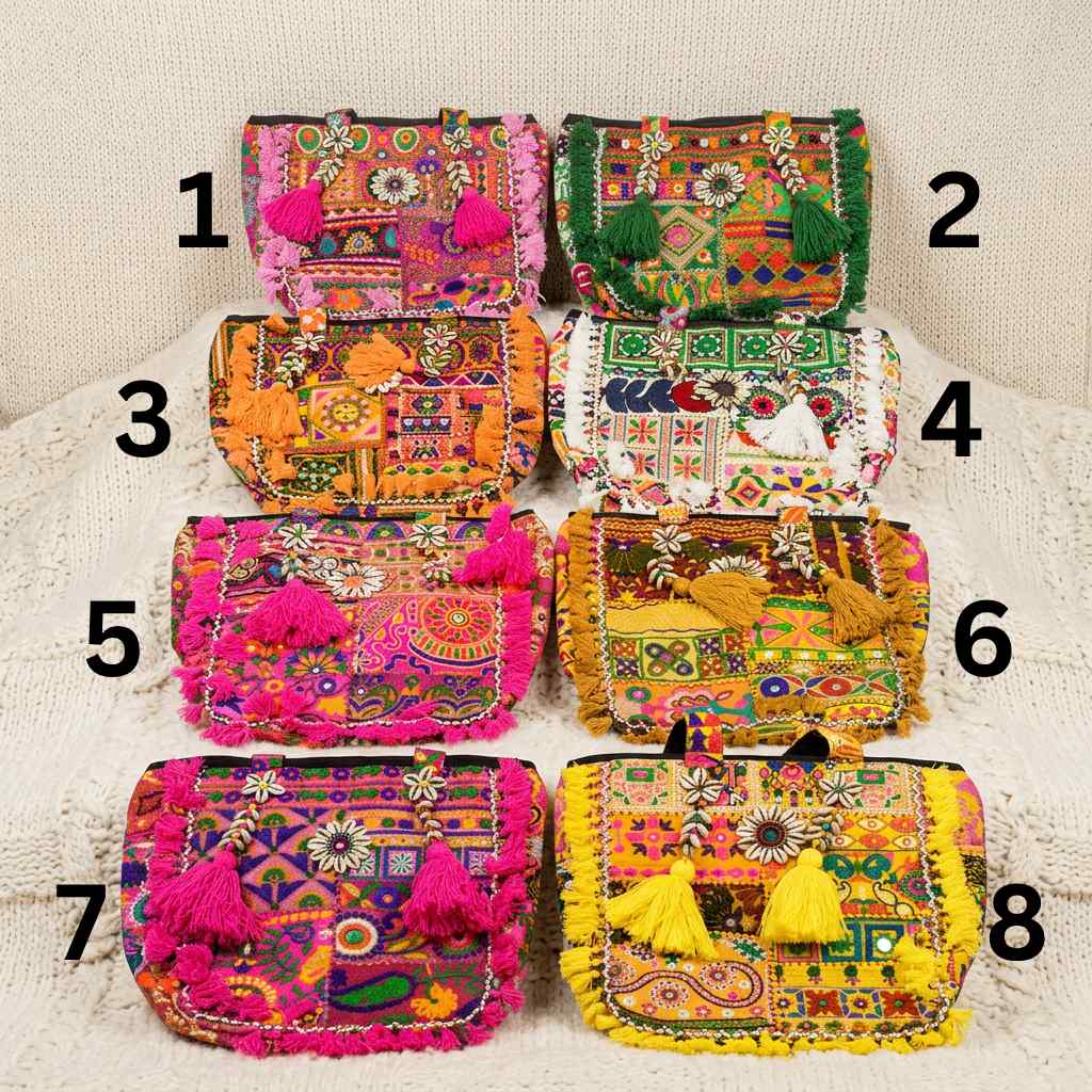 Eight colorful banjara tote bags with intricate patterns and tassels on a textured surface.