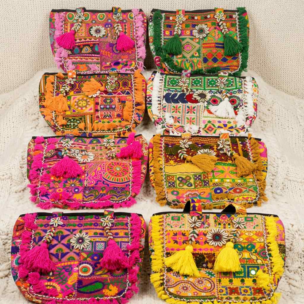 Colorful embroidered banjara tote bags with tassels on a textured surface