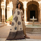Woman in a white traditional outfit with an applique patchwork dupatta standing in front of a marble fountain.