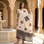 Woman in a white traditional outfit with an applique patchwork dupatta standing in front of a marble fountain.