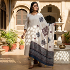 Woman in a white traditional outfit with an applique patchwork dupatta standing in front of a marble fountain.