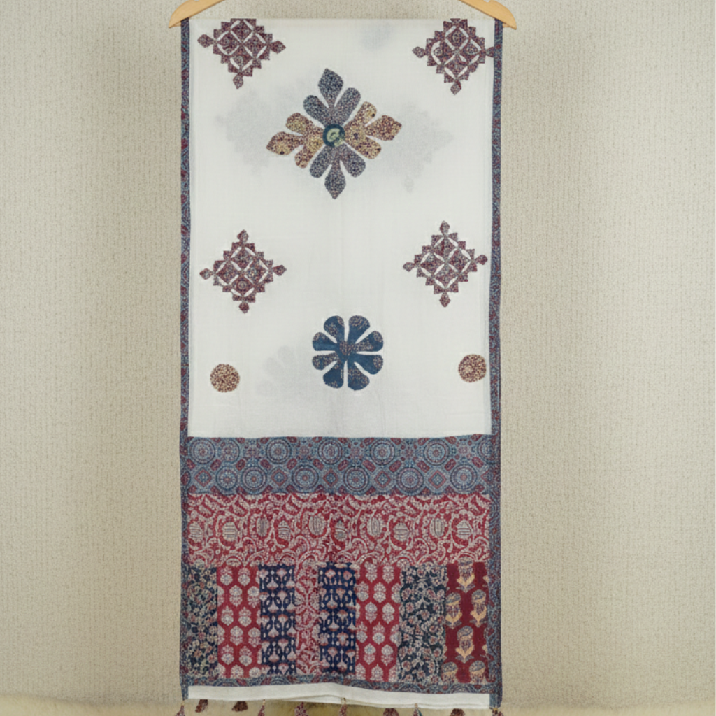 Woman in a white traditional outfit with an applique patchwork dupatta standing in front of a marble fountain.