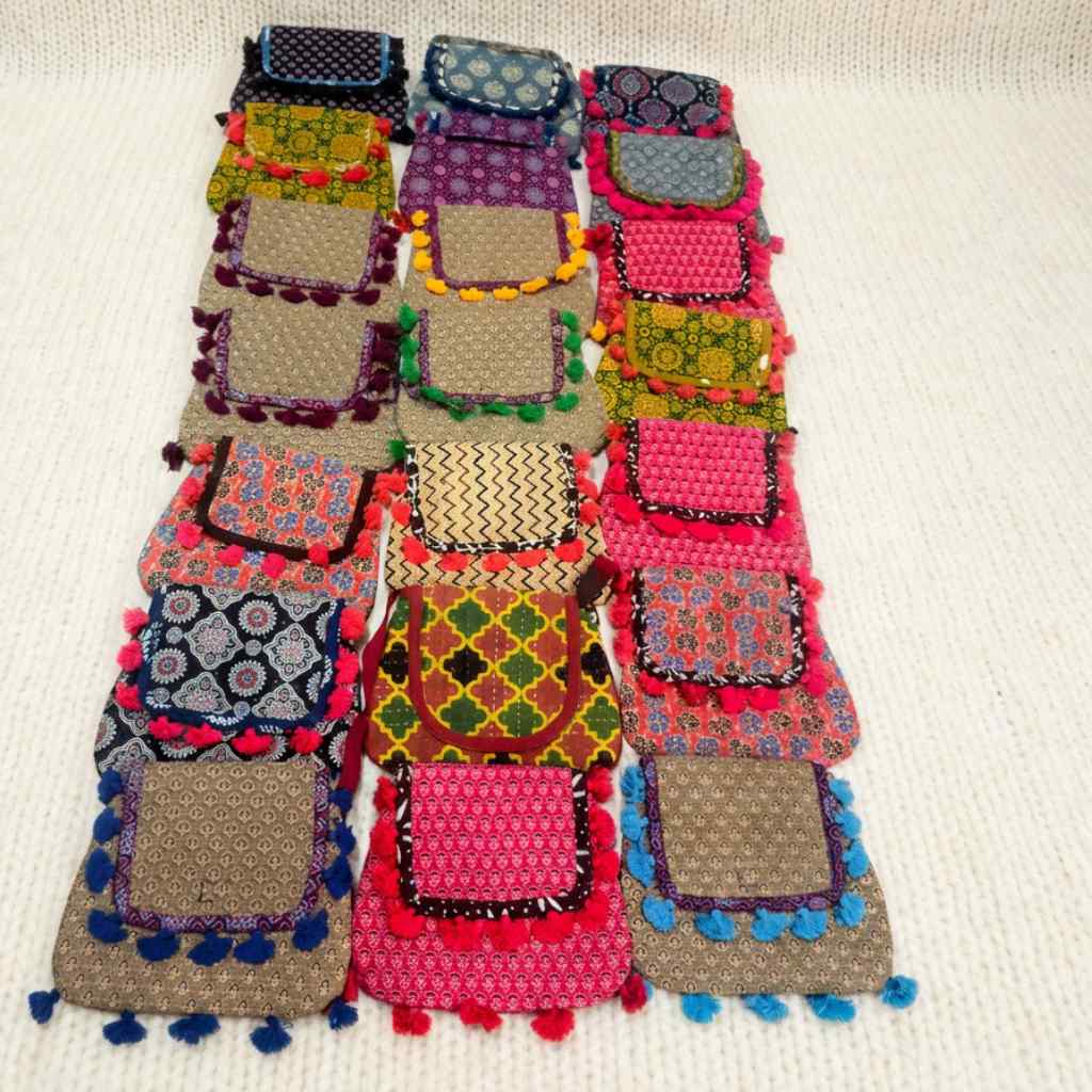 Colorful patchwork bag with patterned sections and pom-pom details on a beige background