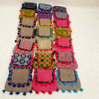 Colorful patchwork bag with patterned sections and pom-pom details on a beige background