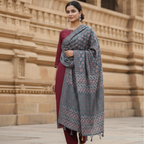 Woman wearing a blue ajrakh dupatta with red kurta set in front of a stone building