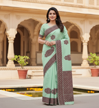Woman in a light green saree with brown patterns standing in front of an architectural background.