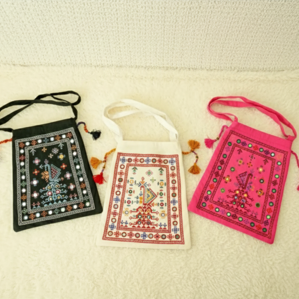 Three embroidered bags in black, white, and pink on a beige background