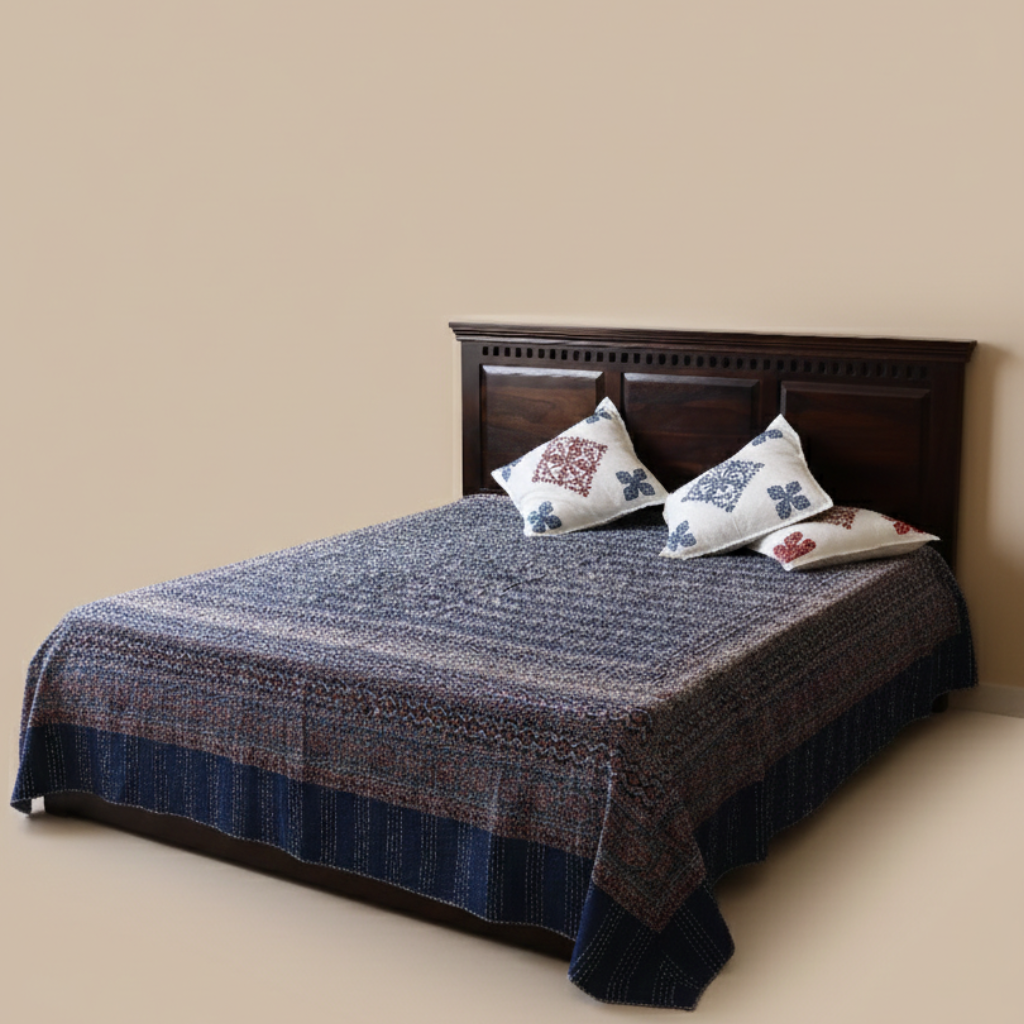 Bed with dark wooden headboard, blue patterned bedsheet, and decorative pillows against a beige wall.