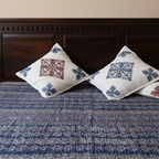 Two embroidered pillows on a blue patterned applique bedspread with a wooden headboard.