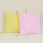 Two applique cushion covers, one yellow and one pink, on a beige surface.
