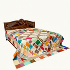 Colorful patchwork quilt on a bed with a wooden headboard against a white background