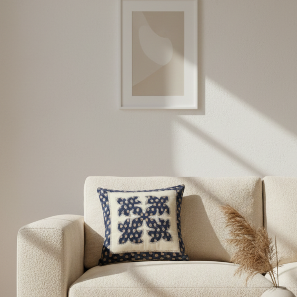 Beige sofa with a decorativeapplique cushion cover and framed artwork on a light wall.