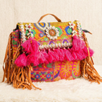 Colorful boho handbag with floral patterns, tassels, and fringes on a textured surface