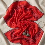 Red embroidery dupatta with black embroidery and silver earrings on a beige fabric background