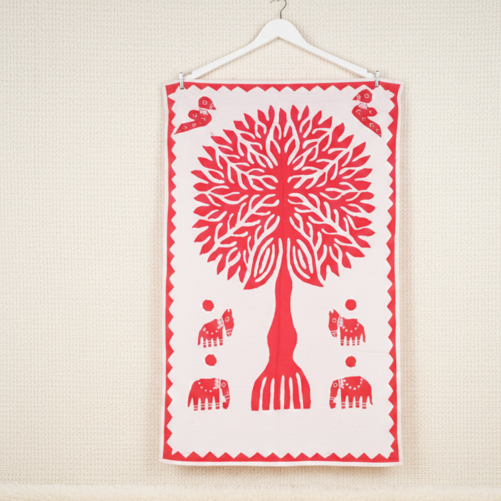 Decorative wall hanging with a red tree design on a white background, hanging on a beige wall.