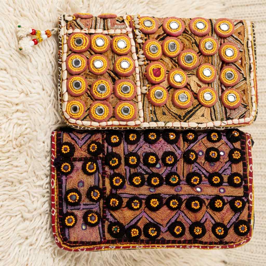Two embroidered zari pouches with intricate patterns on a textured surface.
