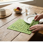 Person placing a green patterned cloth on a wooden table with a bowl of fruit and cups.