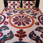 Colorful floral applique bedspread with matching pillows on a bed.