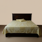Bed with a green tree patterned bedsheet with pillows and dark wooden headboard against a beige wall.