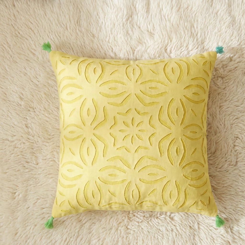 Yellow decorative cushion cover with floral pattern on a beige textured surface