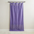 Purple curtain with geometric patterns on a wooden rod against a beige wall.