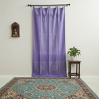 Purple curtain with decorative top hanging on a rod above a patterned rug.