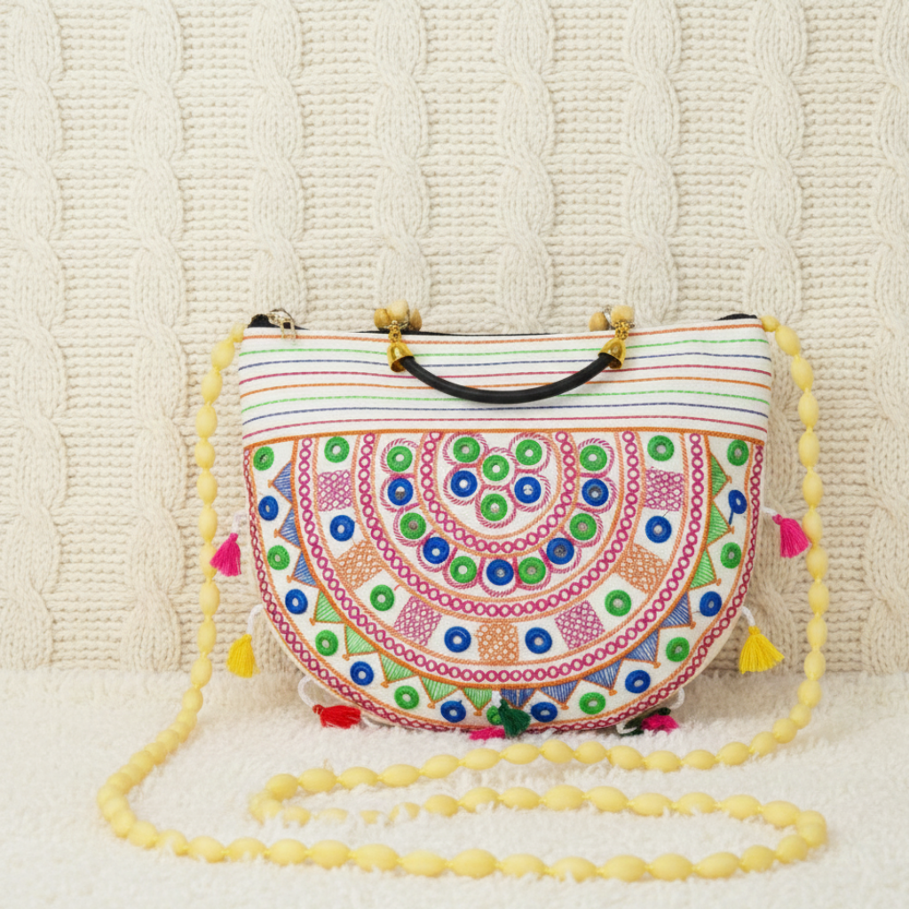 white boho chic sling bag with intricate patterns and tassels on a textured beige background
