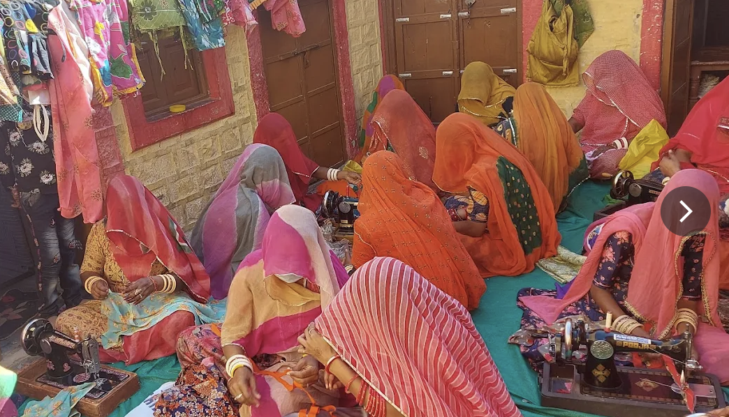 Group of women in colorful traditional attire working on sewing machines in a room.