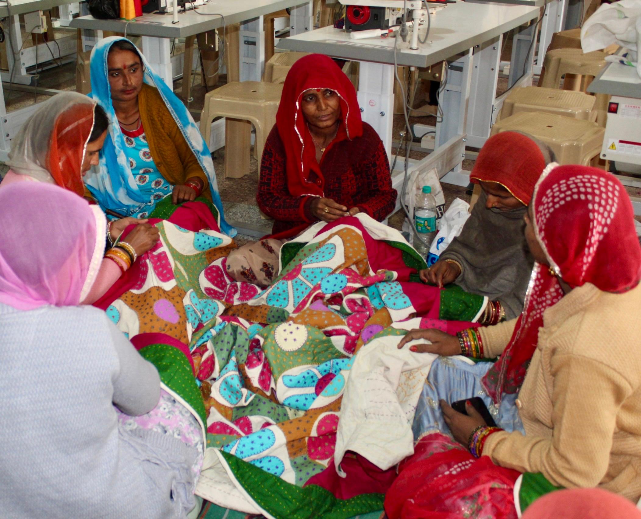 Group of women sitting around a colorful quilt in a workshop setting.