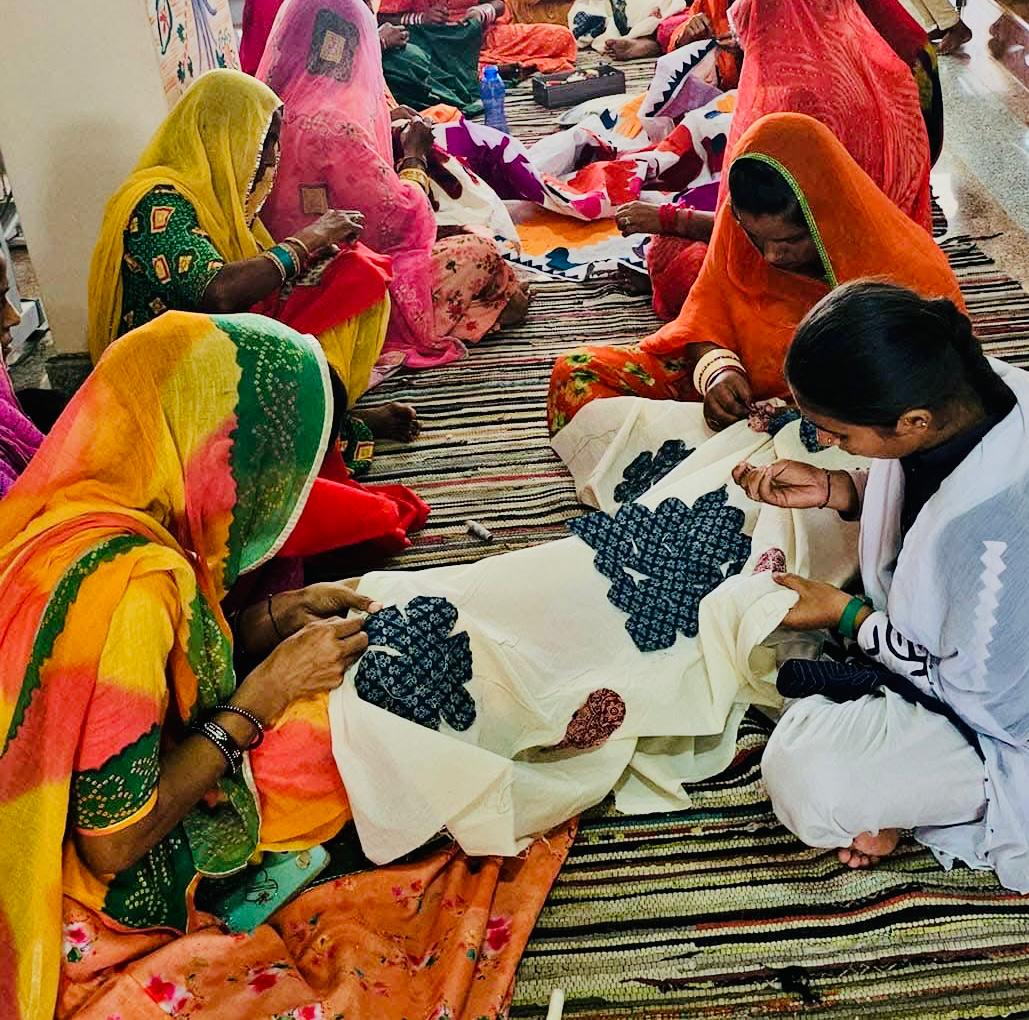 Group of women in colorful traditional attire working on textile items.
